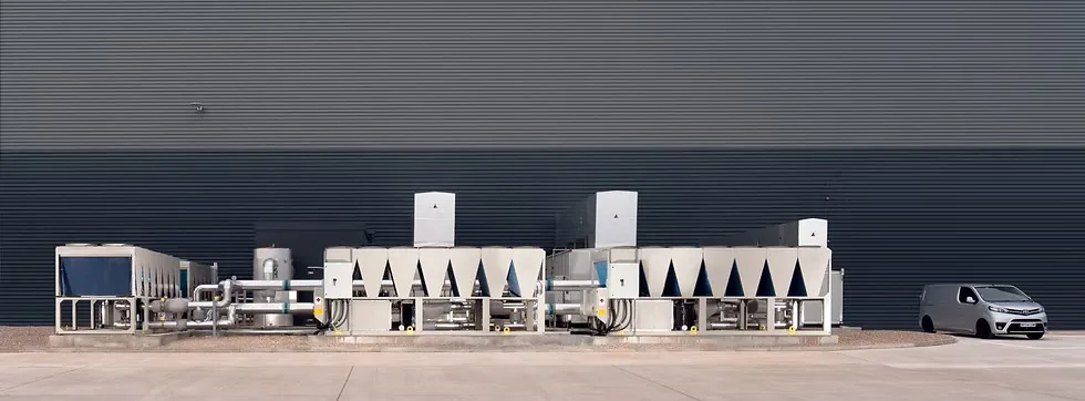 A row of air-cooled chillers and their pipework installed against the wall of a large warehouse