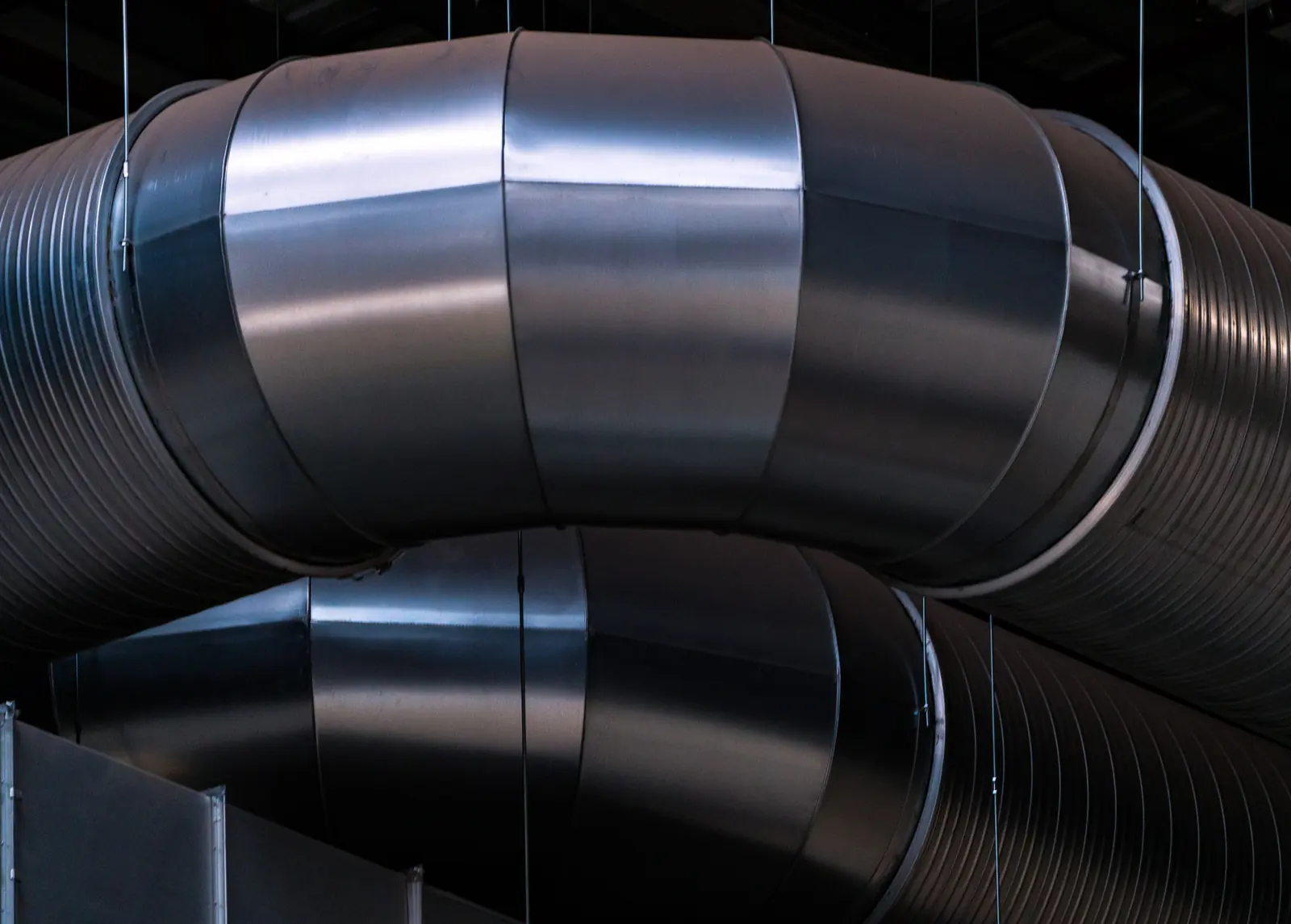 Large spiral ductwork bends hung on rods below a dark ceiling