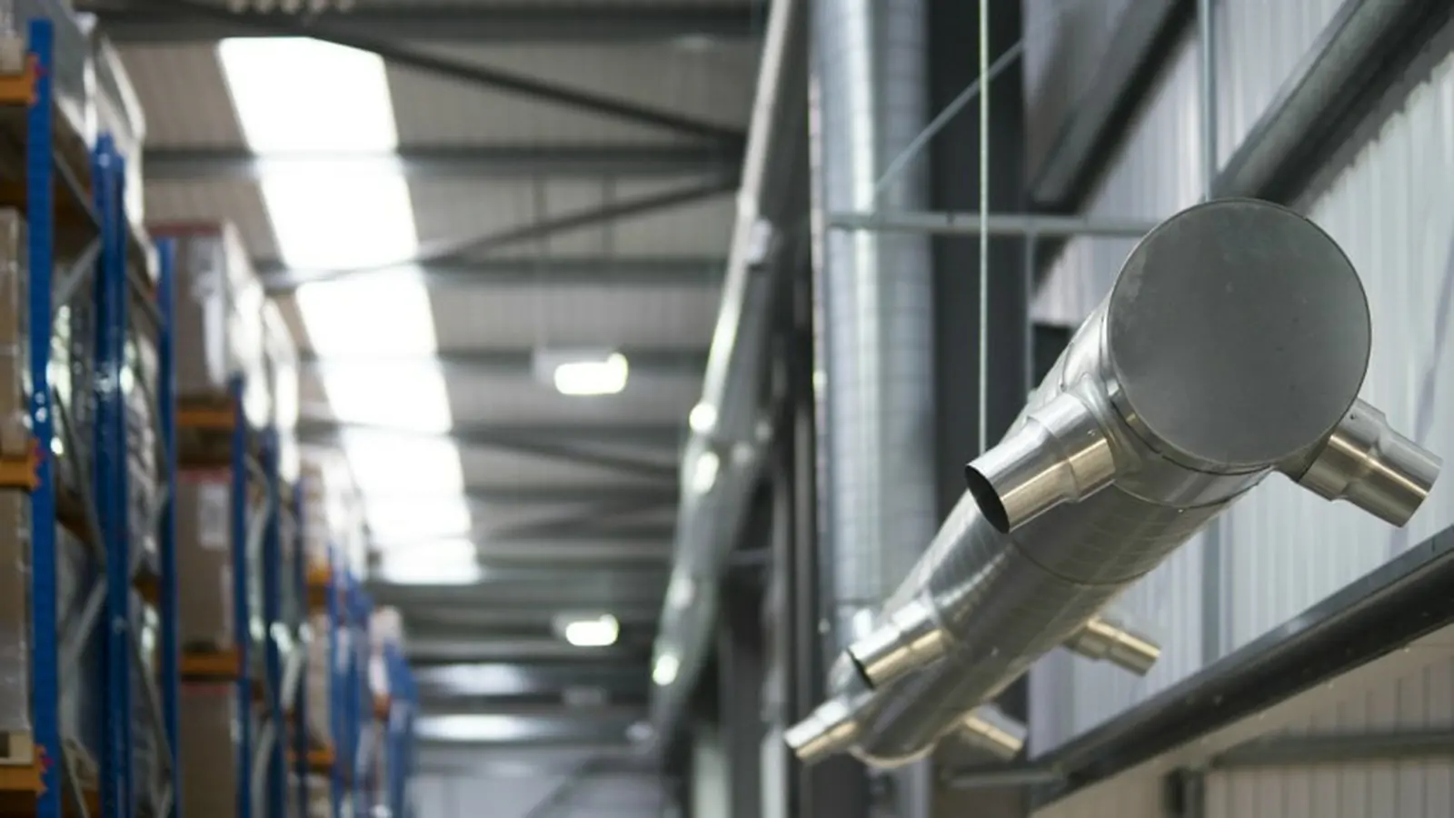 Air induction ductwork with angled nozzles mounted high along a warehouse wall beside pallet racking