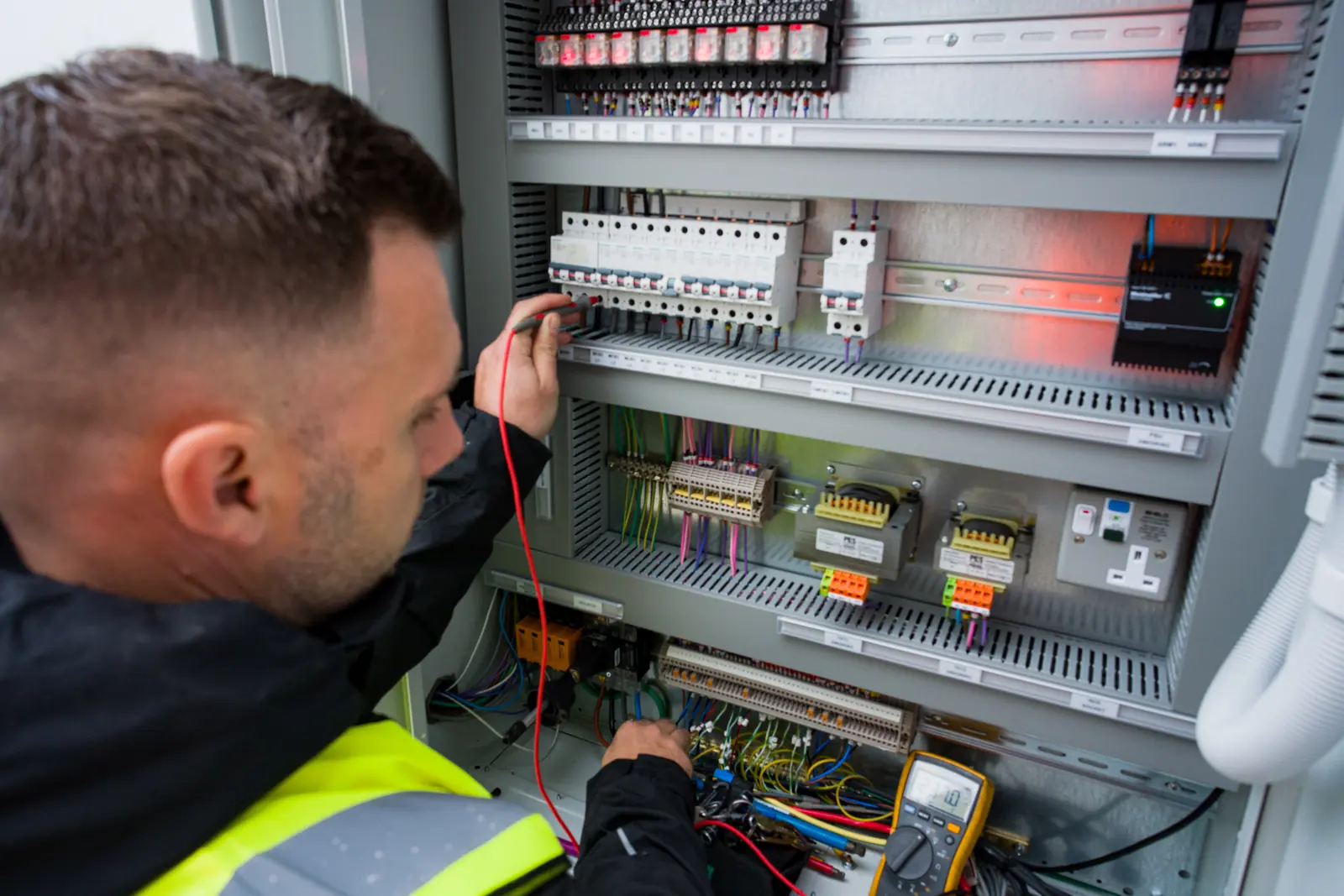 An engineer testing the wiring inside an open electrical control panel with a multimeter