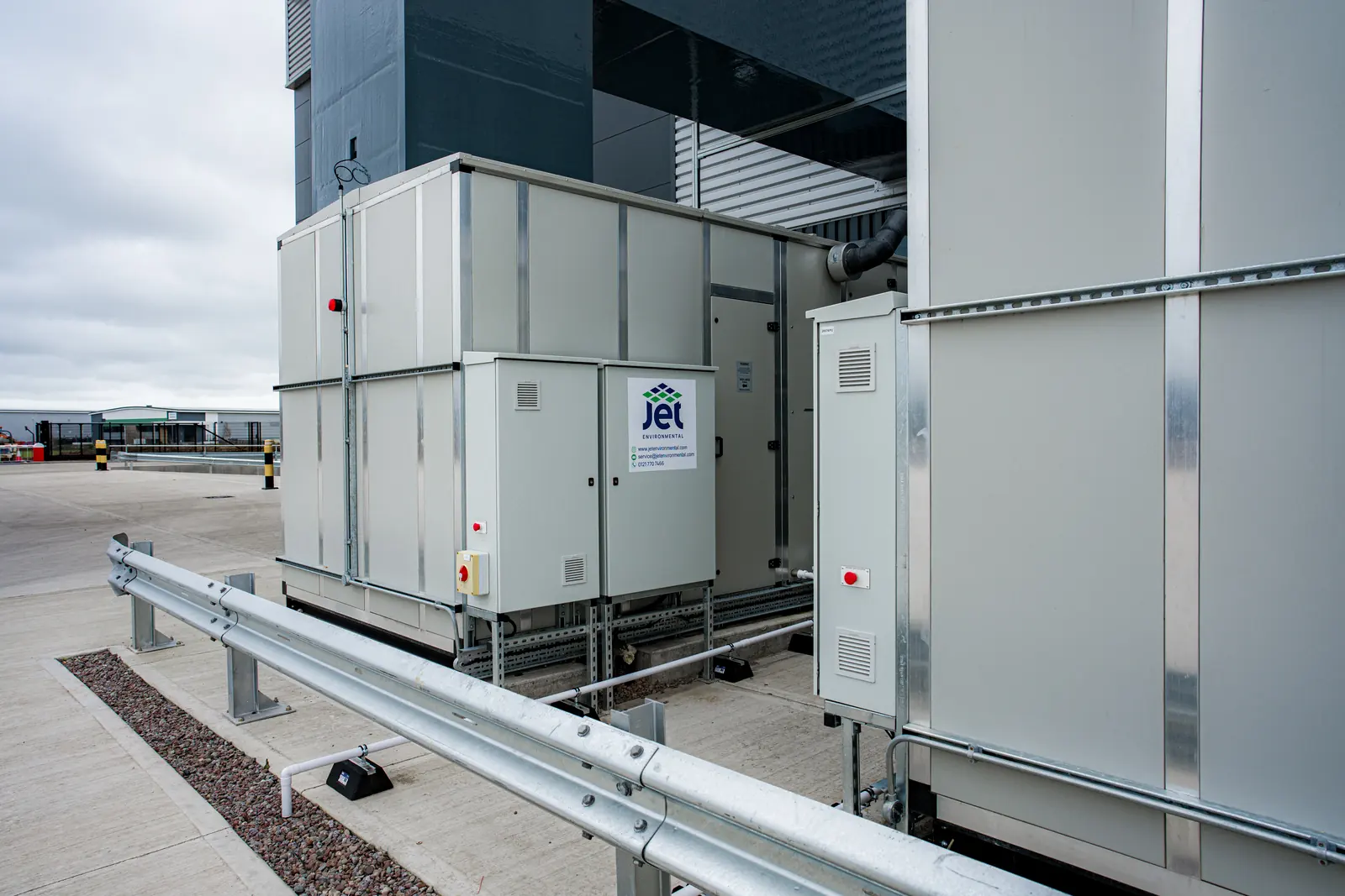 A Jet Environmental air handling unit and control cabinets installed outside a warehouse behind a crash barrier