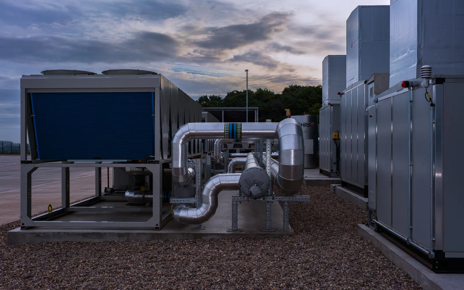 An air-source heat pump and air handling units joined by insulated pipework on an outdoor plant deck at dusk