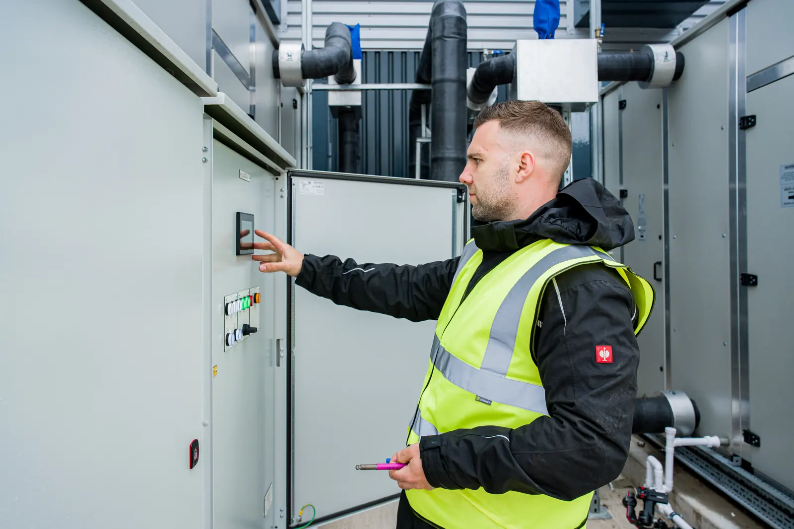 An engineer in a hi-vis vest using the touchscreen controller on an air handling unit control panel